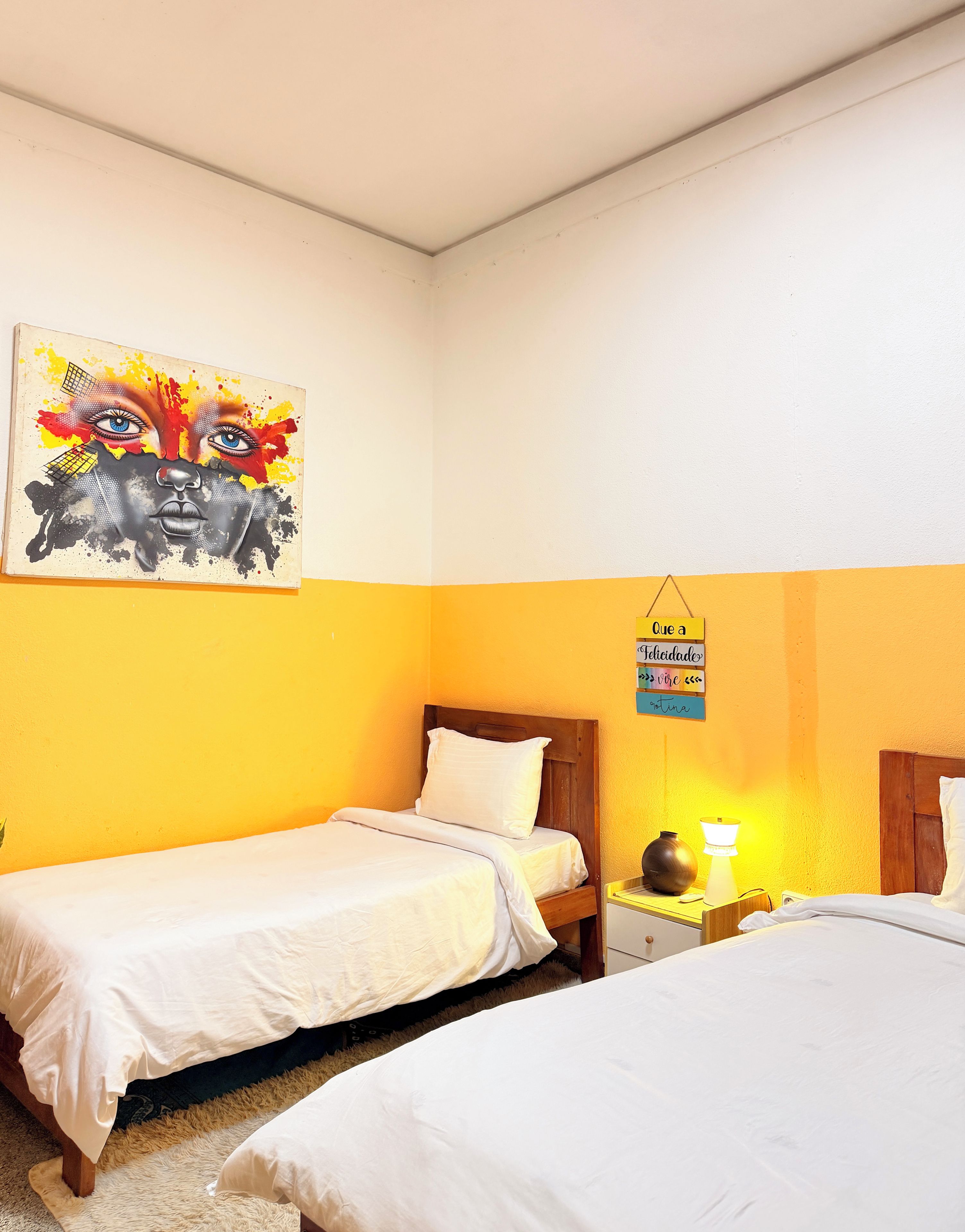 A hotel room with two beds, a painting on the wall, and a sign with a positive message.