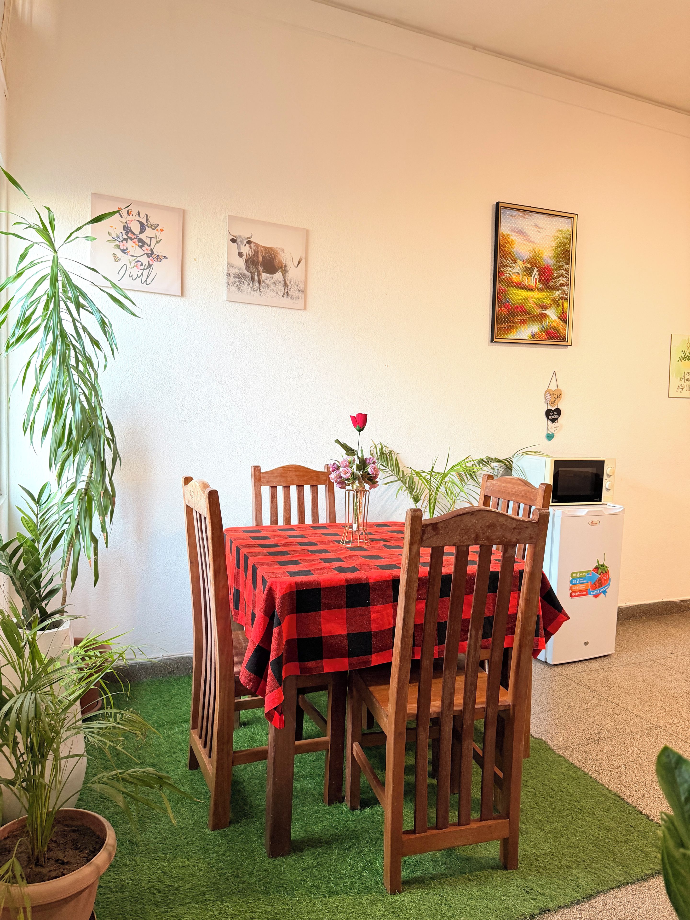 Un comedor con mantel a cuadros rojo y negro, sillas de madera y una mesa pequeña con un jarrón de flores.