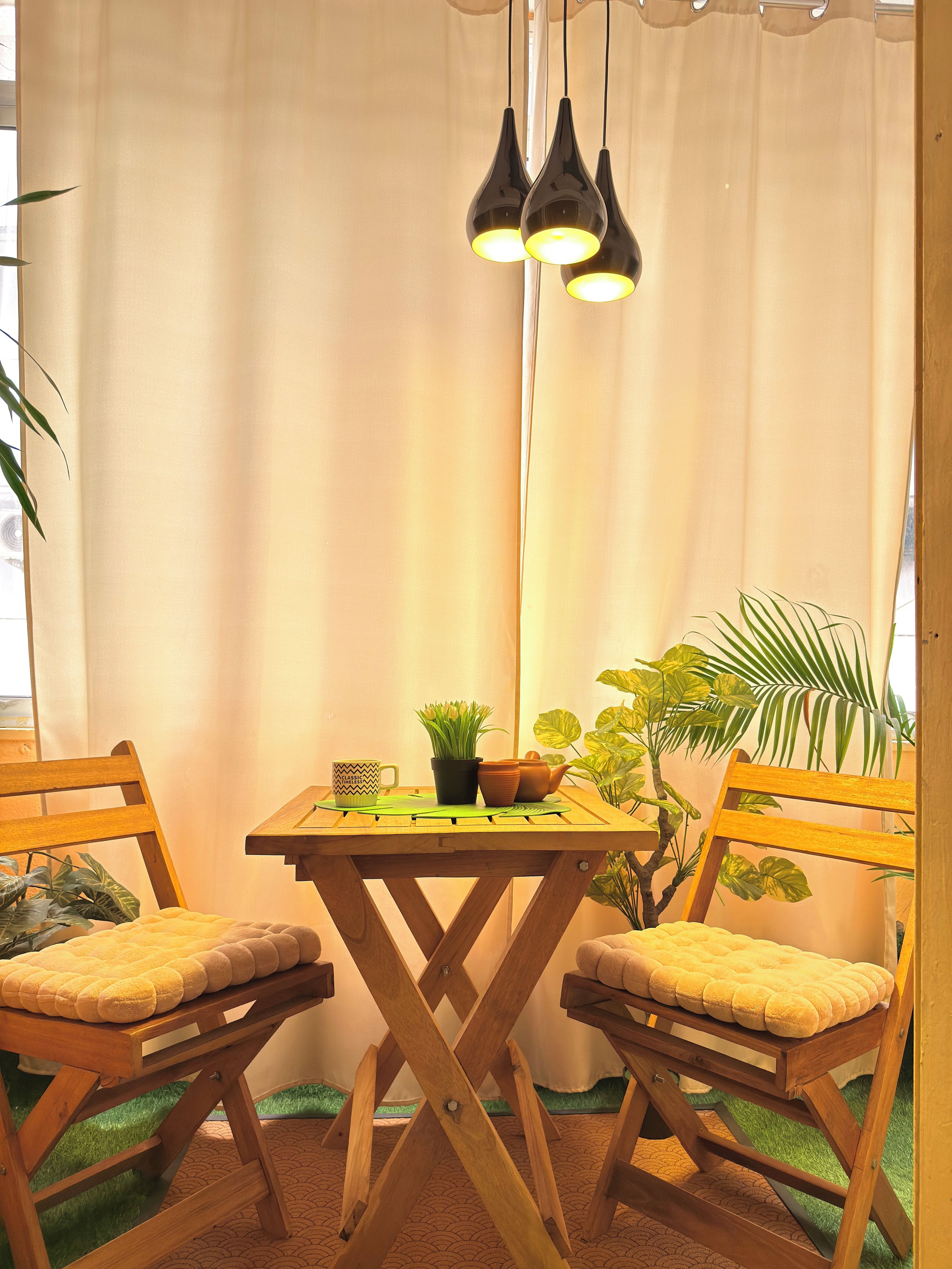 Un rincón acogedor con una mesa y sillas de madera, una planta en maceta y una lámpara colgante.