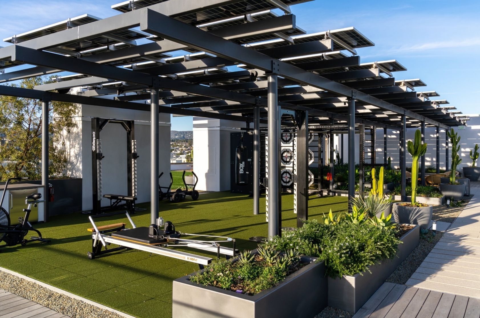 A rooftop gym with exercise equipment, solar panels, and planters.