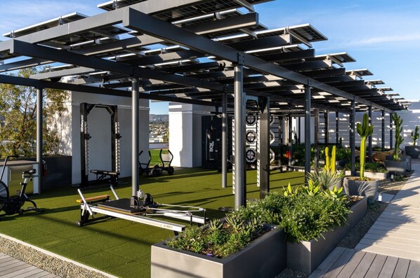 Un gimnasio en la azotea con equipamiento de ejercicio, paneles solares y jardineras.