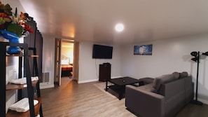 A living room with a sofa, a coffee table, a flat-screen TV mounted on the wall, and a wooden floor. - SHERWOOD ARMS MOTEL_CABIN#5 (Running Springs)