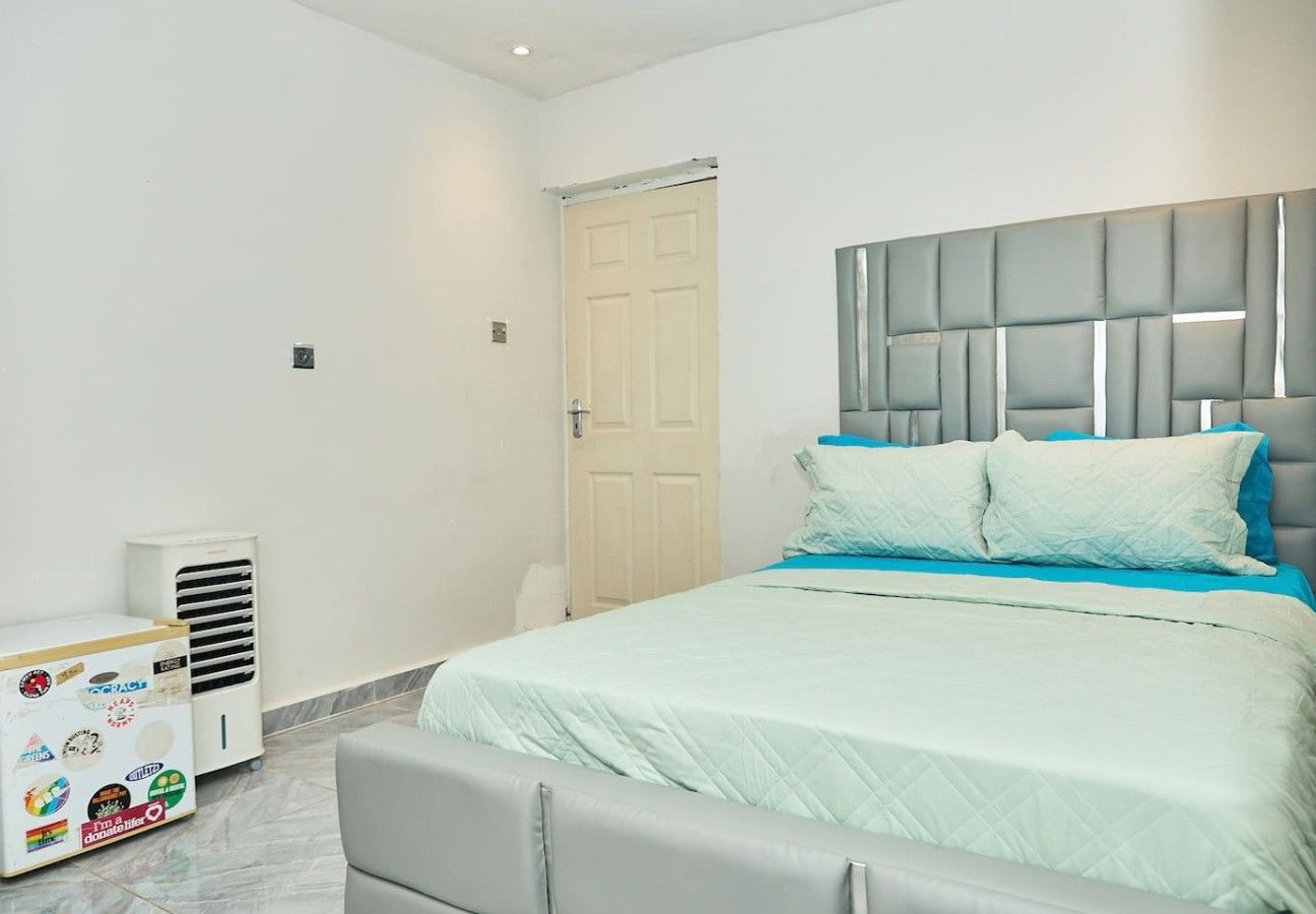 Un dormitorio con una cama, cabecera, una puerta y un equipo de aire acondicionado blanco.