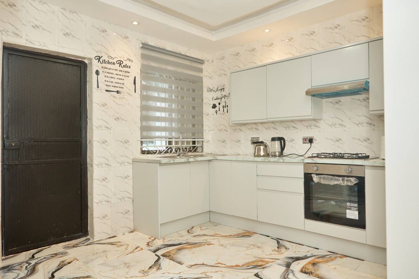 Una cocina moderna con armarios blancos, una puerta negra, un salpicadero de mármol y horno empotrado.