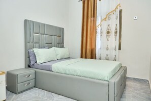 Un dormitorio con cama, mesitas de noche y una cortina.