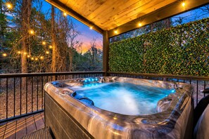 A hot tub with a wooden deck and a hedge wall, surrounded by trees. - Games Inside & Out | Hot Tub | Sleeps 11 (Broken Bow)