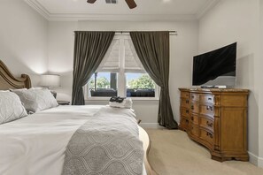Ein Schlafzimmer mit einem großen Bett, einem Schminktisch, einem Fernseher und einem Fenster mit Vorhängen.