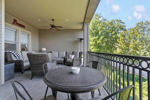 A covered outdoor seating area with a table and chairs, a ceiling fan, and a view of greenery. - Tide on the River | 3BR Condo with Covered Balcony (Tuscaloosa)