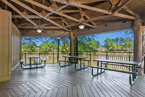 Eine überdachte Terrasse im Freien mit Picknicktischen und einem Geländer mit Blick auf einen Park.