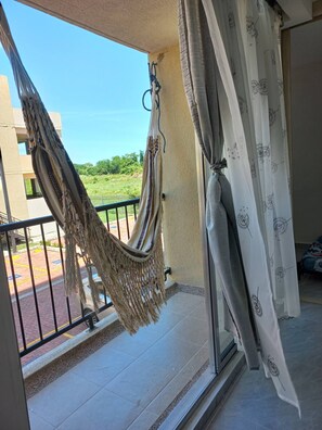 Un balcón con una hamaca, una ventana con cortinas y vistas al verdor.