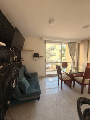 A living room with a sofa, a fan, a TV, and a dining area with chairs and a table. - Lindo Apartamento con Piscina Girardot · Hasta 10 personas (Girardot)