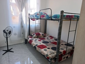 A bunk bed with a patterned bedspread, a standing fan, and a window with curtains. - Lindo Apartamento con Piscina Girardot · Hasta 10 personas (Girardot)
