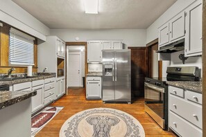 A kitchen with white cabinets, a stainless steel refrigerator, a stove, and a microwave. - Tide & True | 5BR Walk to UA | Prime Location (Tuscaloosa)
