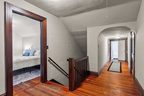 A narrow hallway with wooden flooring and a sloped ceiling. - Tide & True | 5BR Walk to UA | Prime Location (Tuscaloosa)