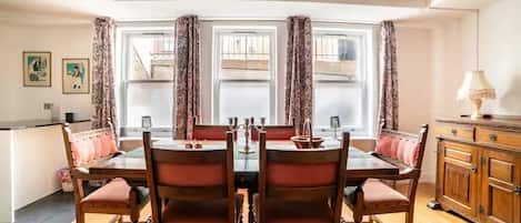 A dining area with a wooden table and chairs, a cabinet, and a view through large windows.