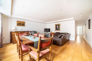 A spacious living room with a wooden dining table, leather sofa, and a television. - Apartment Sleeps 4 Near Windsor Castle (Windsor)