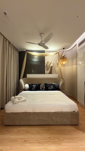 A modern bedroom with a large bed, a ceiling fan, and a wardrobe. - Luxury Paradise Studio Apartment | Elegant & Peaceful Stay (Gurugram)
