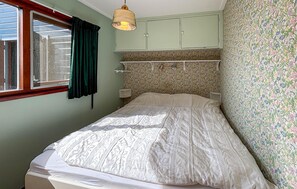 A bedroom with a bed, a window with curtains, a hanging lamp, and floral wallpaper.