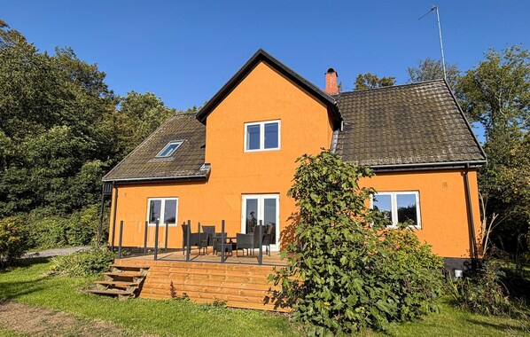 Ein zweigeschossiges Haus mit einem geneigten Dach, einer Holzterrasse und einem Schornstein.