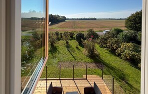 A view from a balcony with a wooden deck, overlooking a landscaped garden and a field. - Amazing home in Nexø with WiFi (Nexø)