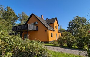 Ein zweistöckiges Haus mit Balkon, umgeben von viel Grün.