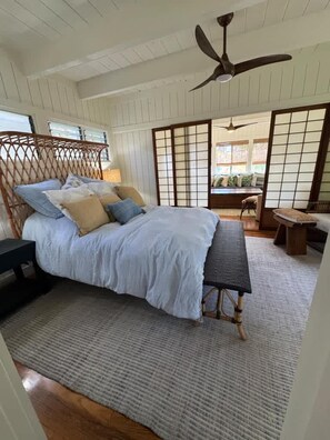 Quarto com cama, um banco, ventoinha no teto e vista através de uma divisória shoji.