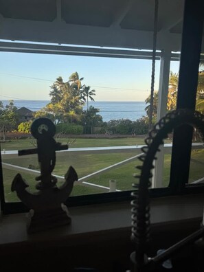Janela com vista para uma área gramada e palmeiras, uma âncora decorativa e um objeto em espiral.