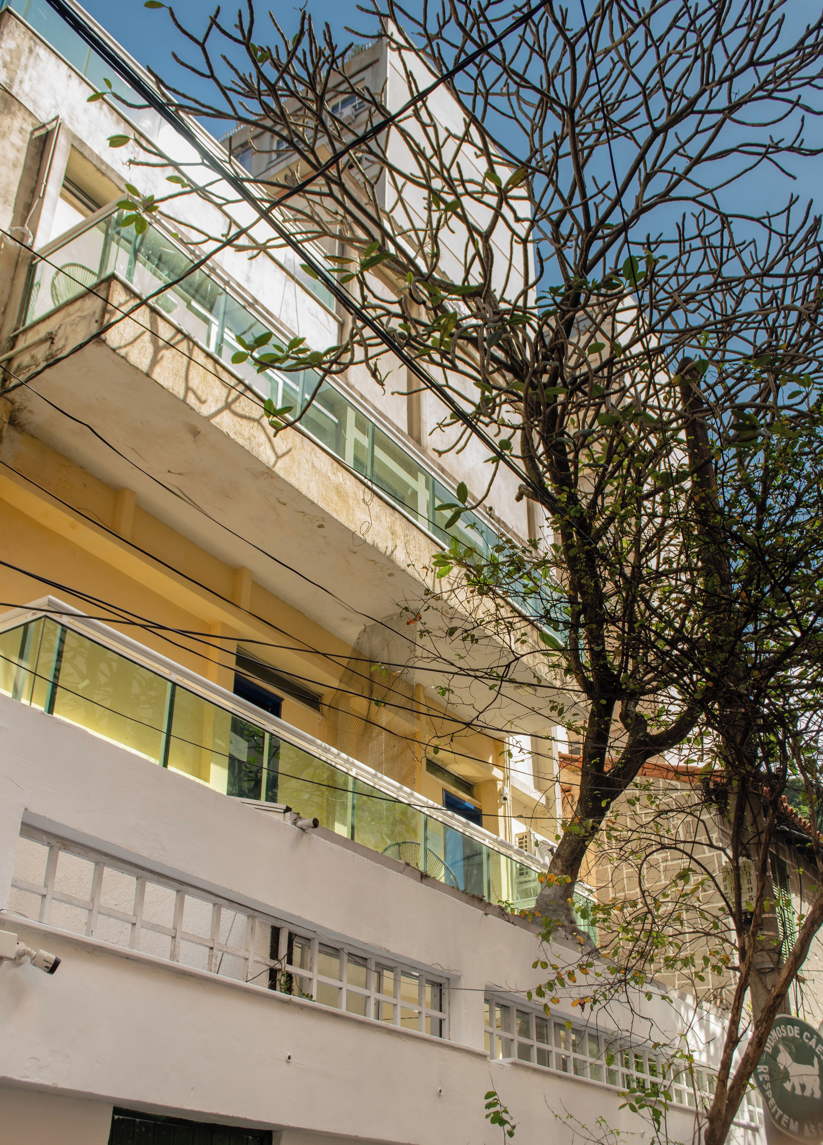 Un immeuble à plusieurs étages doté de balcons, avec un arbre au premier plan et un ciel dégagé.