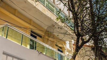 Un immeuble à plusieurs étages doté de balcons, avec un arbre au premier plan et un ciel dégagé.