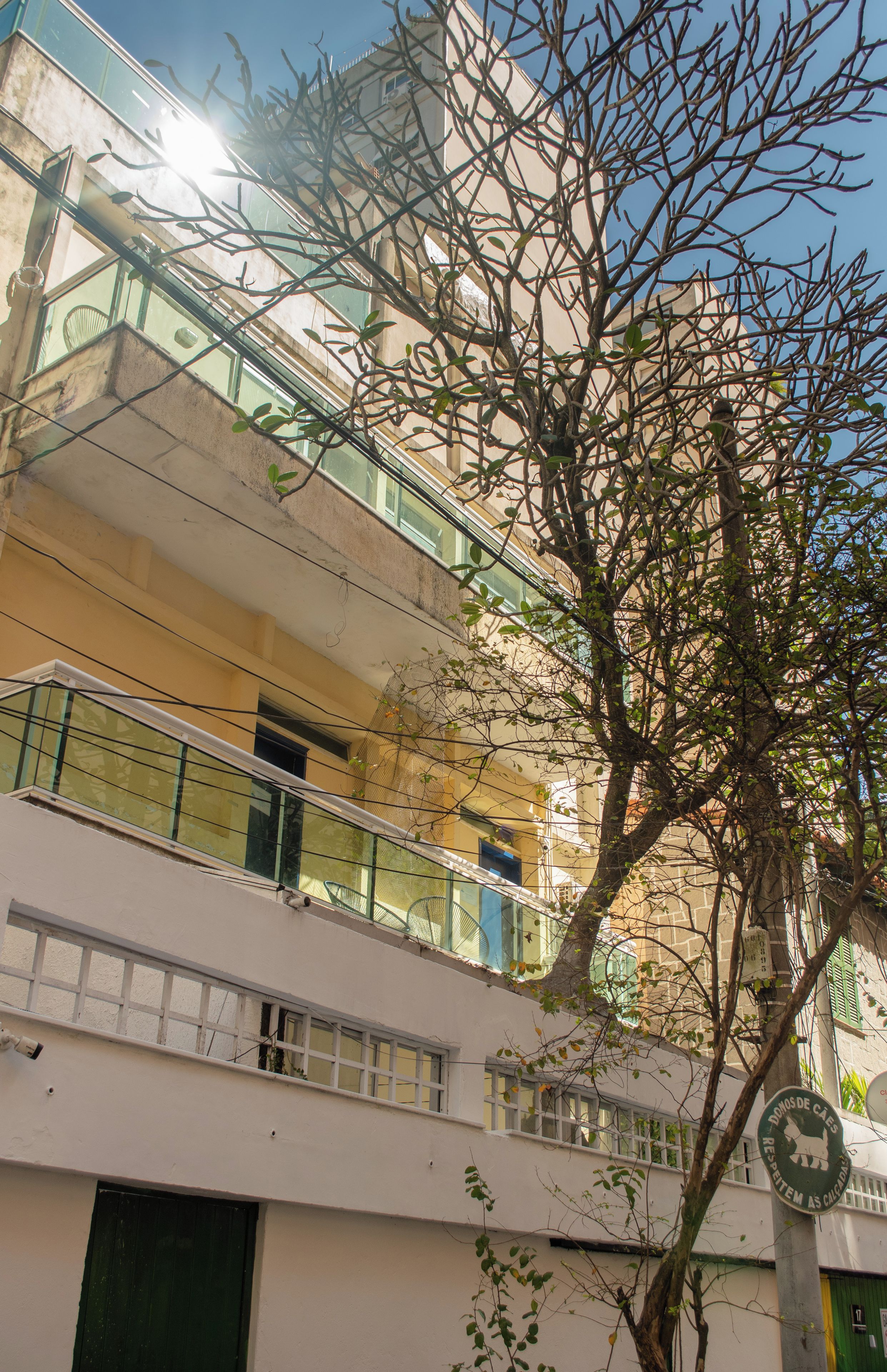 Un immeuble à plusieurs étages doté de balcons, un arbre au premier plan et une enseigne avec du texte.