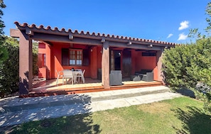 A red building with a covered patio, a table, and chairs. - 2 bedroom cozy apartment in Costa Rei (Costa Rei)