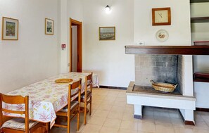 Un coin repas avec une table et des chaises, une cheminée avec un porte-bois, et des tableaux encadrés accrochés au mur.