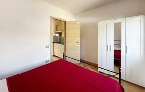 A bedroom with a bed, a wardrobe, and a kitchen area visible through an open door. - 1 bedroom amazing apartment in Costa Rei (Costa Rei)