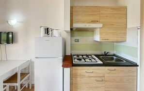 A compact kitchen with a white refrigerator, a stove, and wooden cabinets. - 1 bedroom amazing apartment in Costa Rei (Costa Rei)