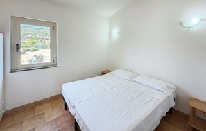 A bedroom with a bed, a window, a nightstand, and a wall-mounted light fixture. - 1 bedroom lovely apartment in Costa Rei (Costa Rei)