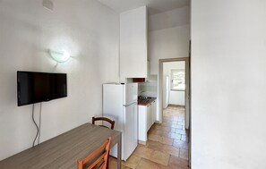 Cuina compacta amb zona de menjador, un televisor de pantalla plana penjat a la paret i vista cap a l'espai saló adjacent.