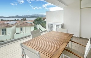 A balcony with a wooden table and chairs, overlooking a lake and buildings. - Beautiful apartment in Cannigione with house sea view (Cannigione)