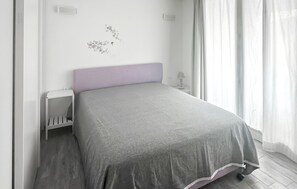 Een slaapkamer met een bed, nachtkastje, lamp en een decoratie aan de muur.
