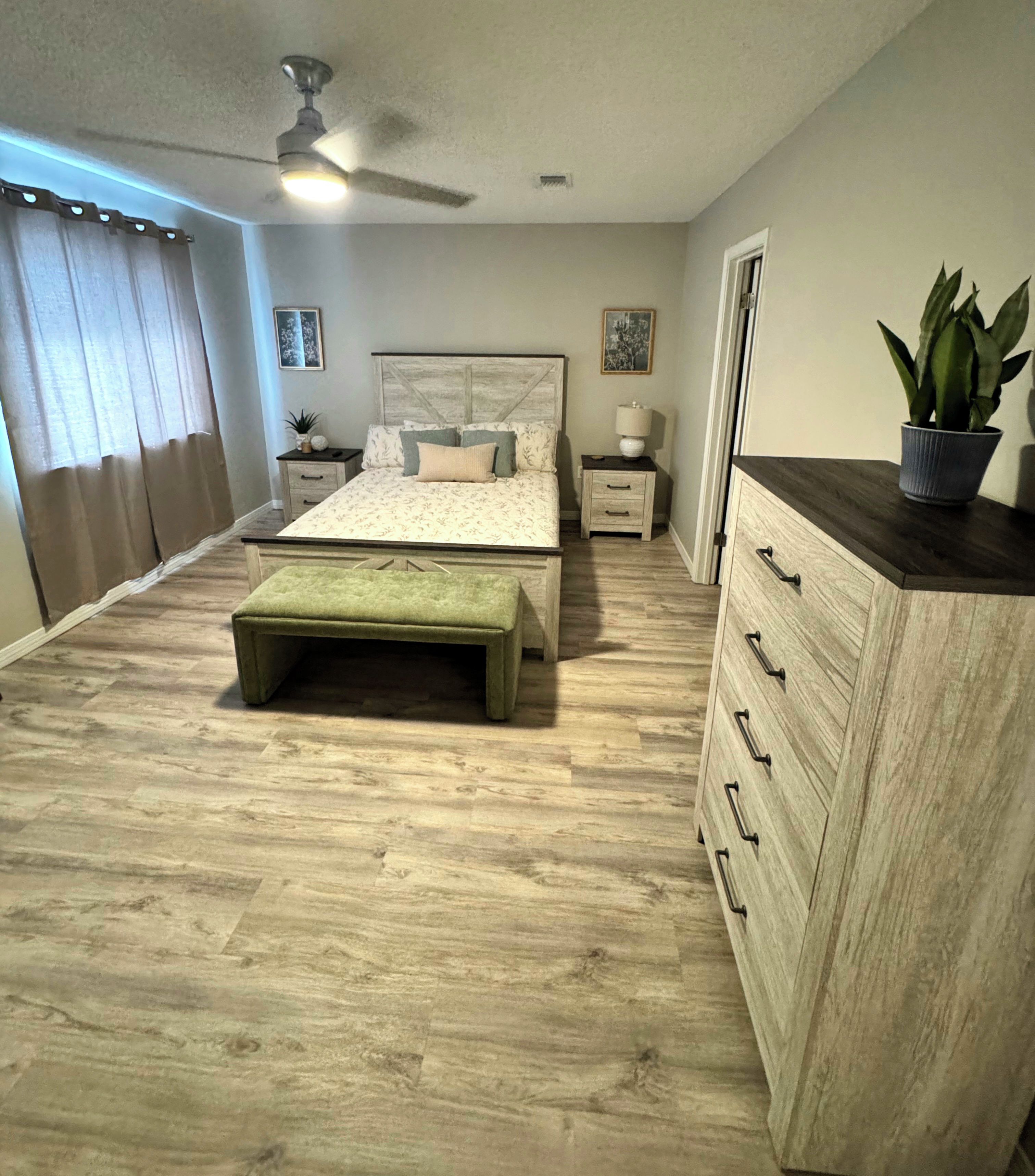 Une chambre à coucher comprenant un lit, des tables de chevet, une commode, un banc, une commode à tiroirs et un ventilateur de plafond.