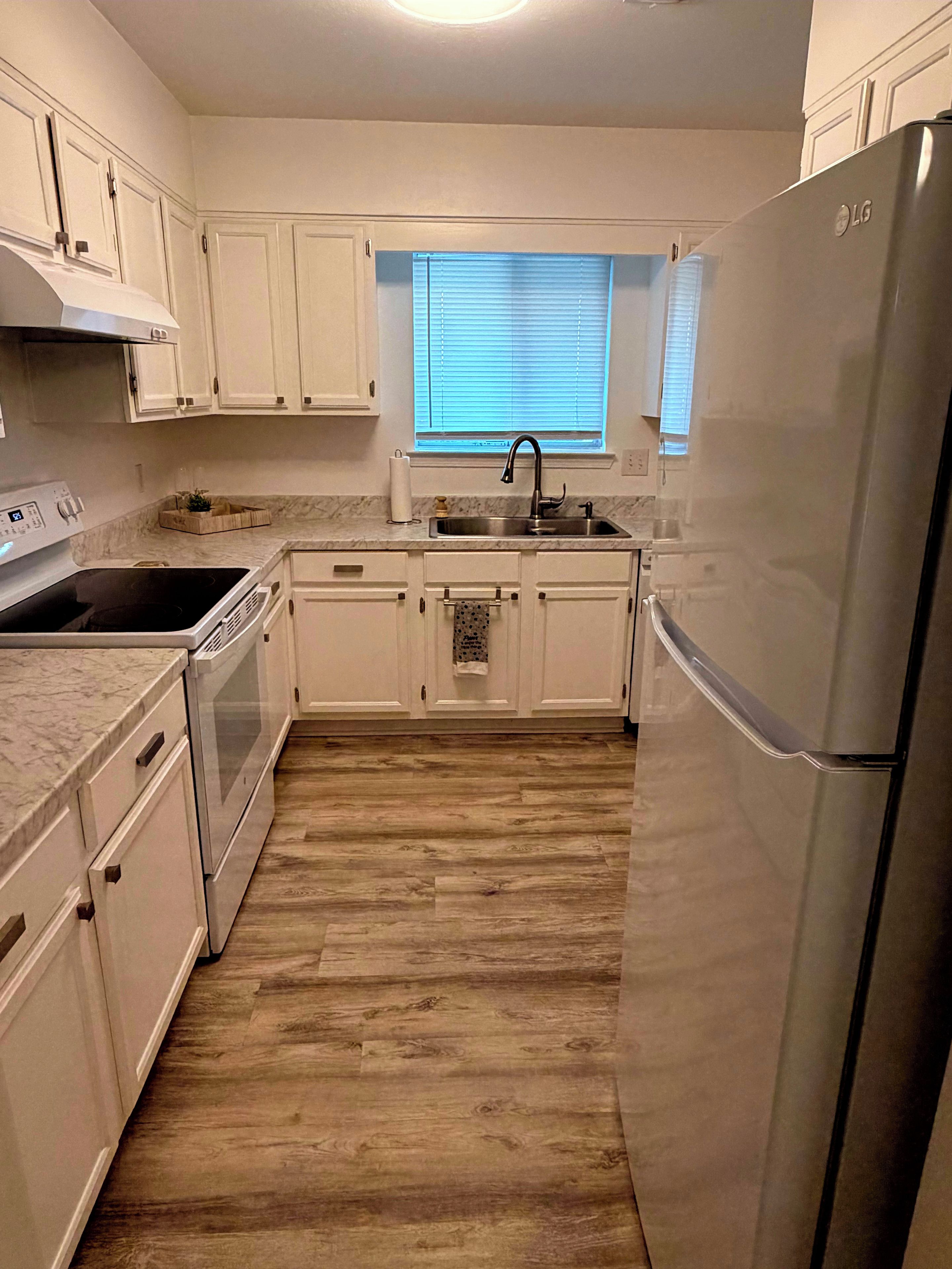 A kitchen with white cabinets, a stainless steel refrigerator, and a window with blinds.