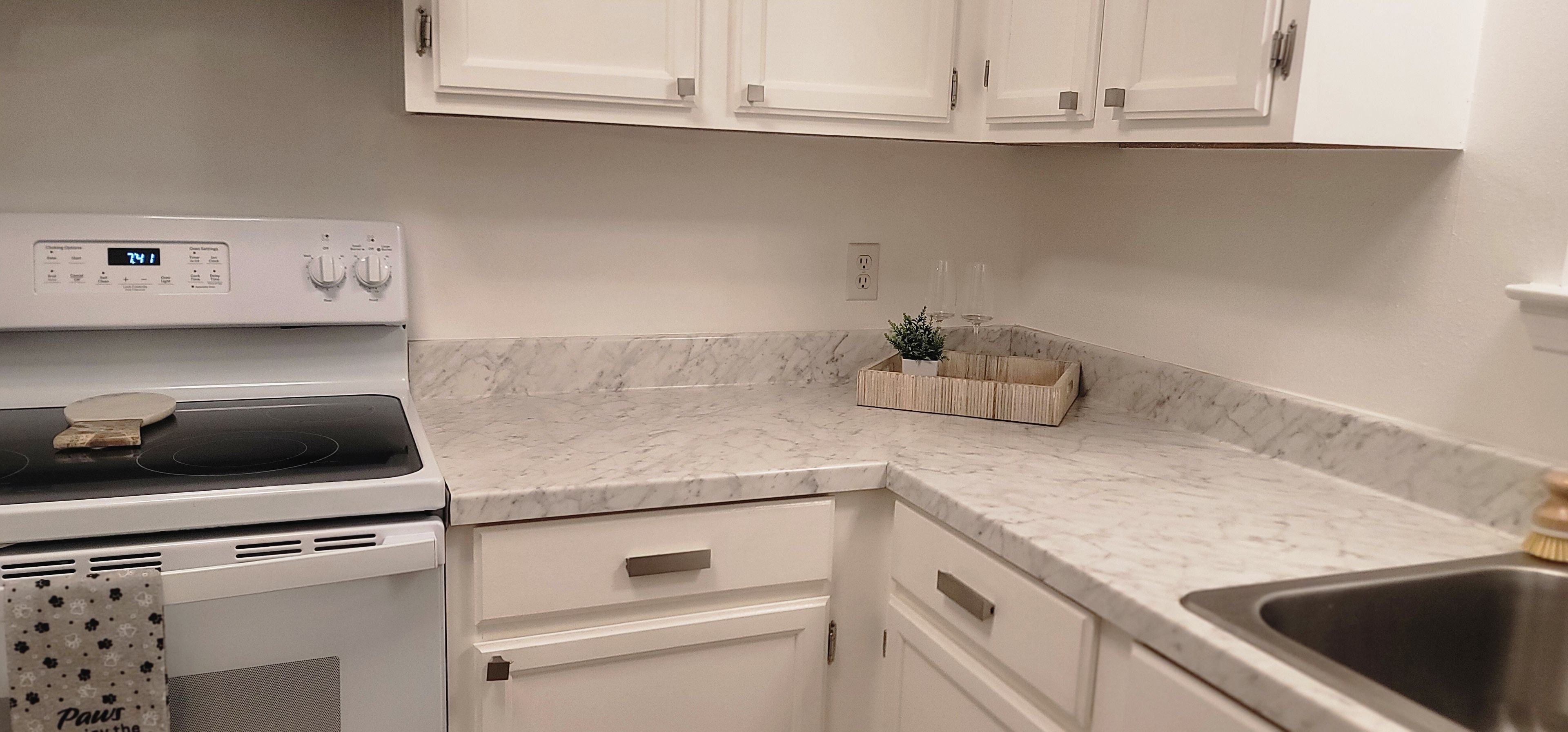 Una cocina con estufa blanca, encimera de mármol y alacenas blancas.