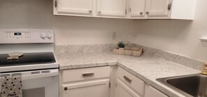 A kitchen with a white stove, a marble countertop, and white cabinets.