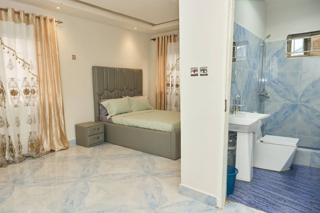 A bedroom with a bed, nightstand, and a bathroom with a sink and shower.