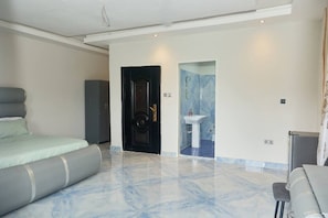 A bedroom with a bed, a wardrobe, a door leading to a bathroom, and a small table. - Spacious 4 Bed Apartment (Freetown)