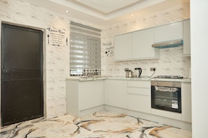A modern kitchen with white cabinetry, a black door, a marble backsplash, and a built-in oven. - Spacious 4 Bed Apartment (Freetown)