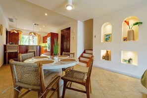 Un coin repas avec une table ronde, des chaises en osier et une cuisine en arrière-plan.