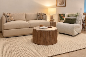 Sala de estar com sofá, poltrona, mesa de centro redonda de madeira e luminária.