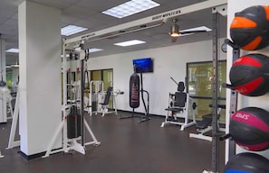 Un gimnasio con diversos equipos de ejercicio, incluyendo una estructura para sentadillas, una prensa de banca y sacos de boxeo.