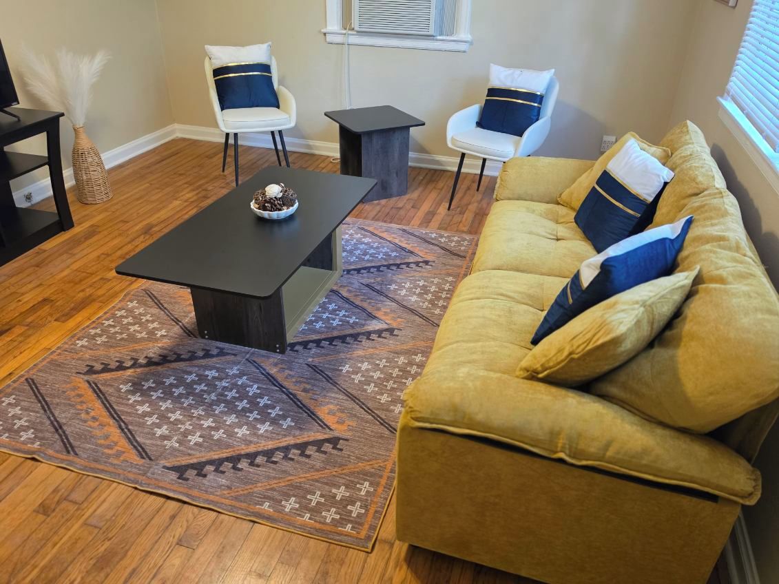 A living room with a sofa, two chairs, a coffee table, and a patterned rug.