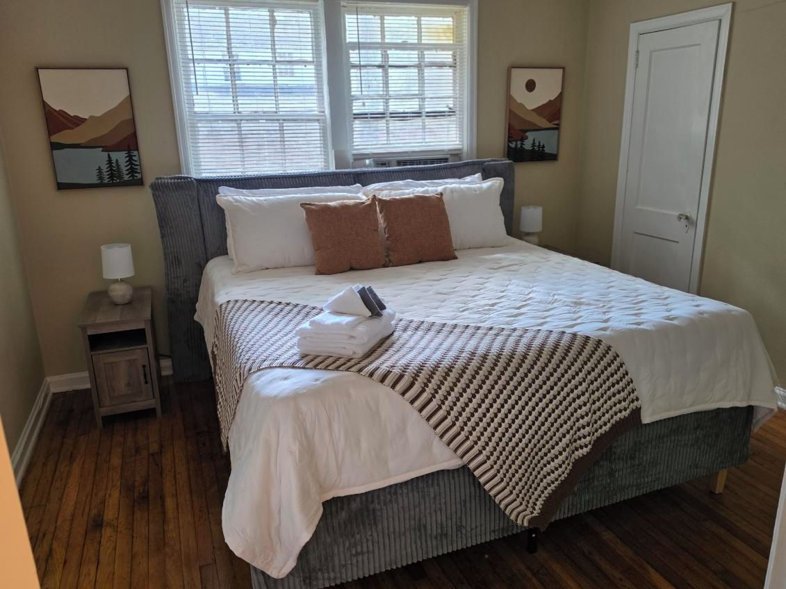A bedroom with a bed, bedside tables, a door, and artwork on the walls.